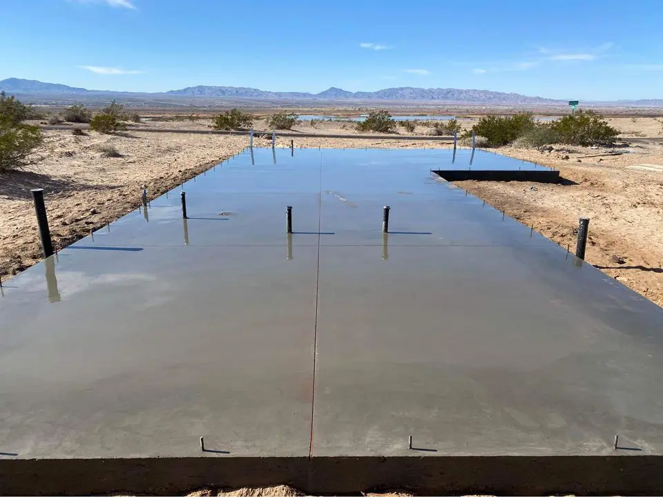 In the desert landscape of Tolleson, AZ, a smooth concrete foundation slab lies amidst sparse vegetation. Mountains loom in the background under a clear blue sky, showcasing the craftsmanship of skilled concrete contractors adept in both residential and commercial projects.