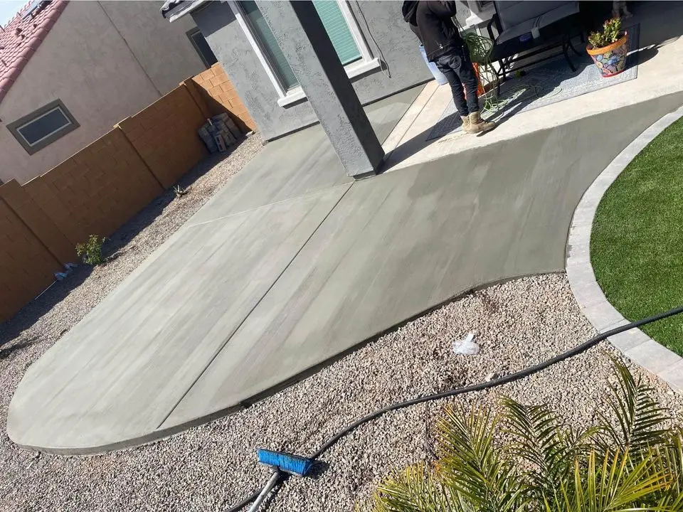 A backyard in Buckeye AZ showcases a concrete patio with a hexagonal pattern crafted by skilled concrete contractors. Nestled beside a stone wall, it offers views of trees and a wheelbarrow under the clear blue sky.