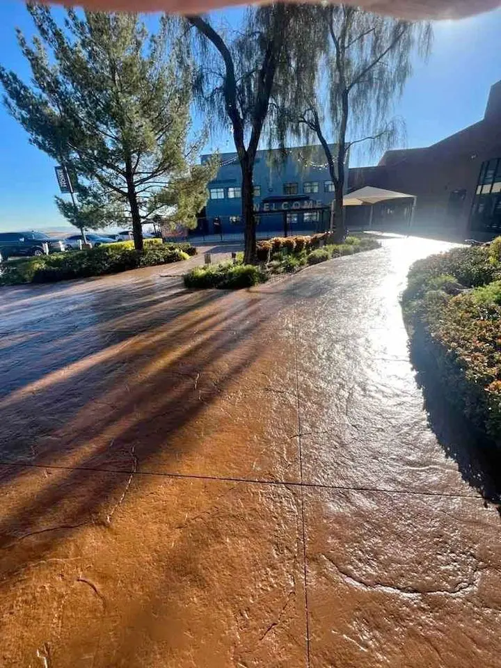 Sunlit pathway with trees casting long shadows leads to a building showcasing a Welcome sign. Beneath the vivid blue skies, it hints at the skilled work of a concrete driveway contractor in Buckeye AZ, offering free quotes for transformative outdoor spaces.